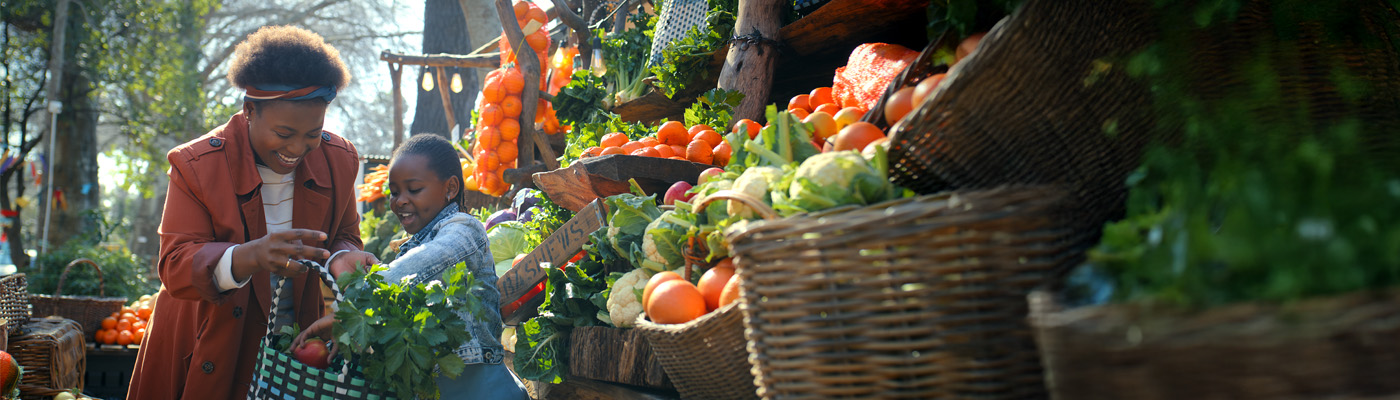 Adult and child putting fresh apples into a blew and white basket at an outdoor produce stand